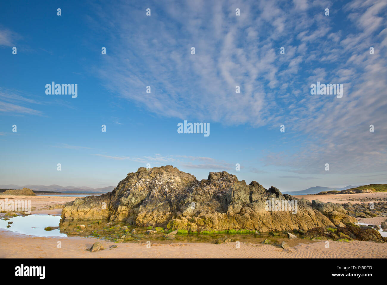 Spiaggia vuota, Ynys Llanddwyn (isola di marea, Anglesey, Galles) con grandi rocce scoscese & piscine di roccia. Cielo blu e wispy cirrus nubi atmosferiche sulla costa. Foto Stock