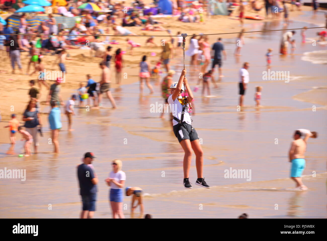 Una donna in un imbragatura viaggia lungo una zip wire sulla spiaggia a mentre le famiglie godono di una giornata soleggiata settembre sulla spiaggia a Bournemouth, Regno Unito Foto Stock