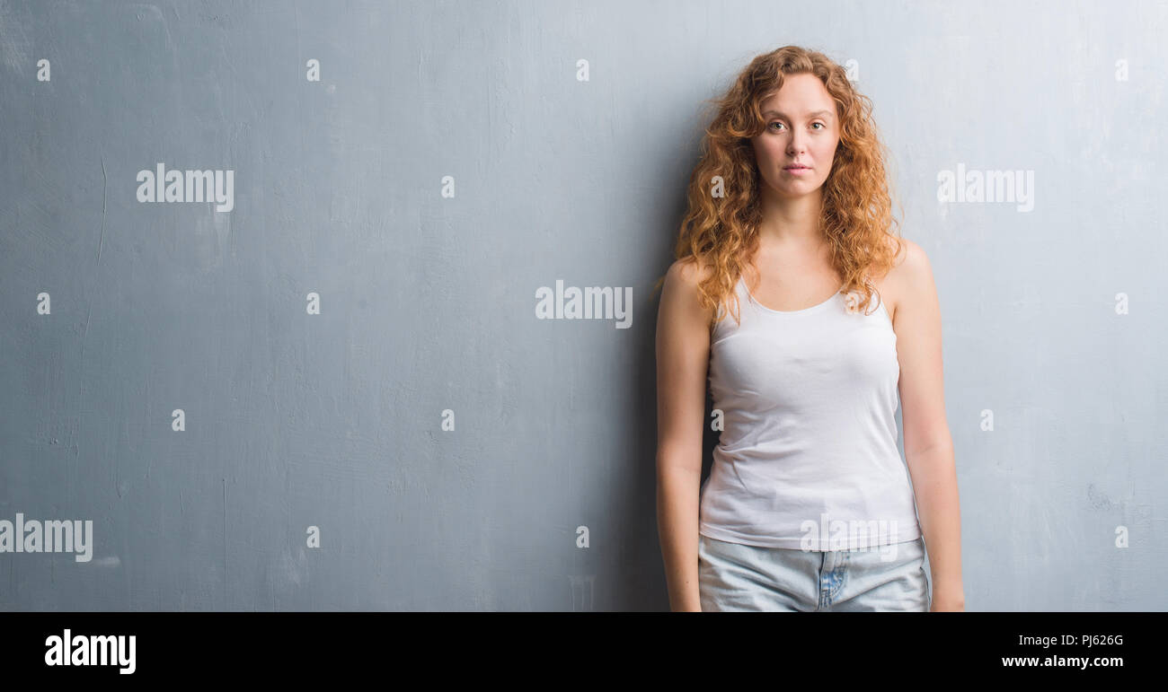 Giovane donna rosso su grigio parete grunge con un fiducioso espressione sul viso intelligente pensare grave Foto Stock