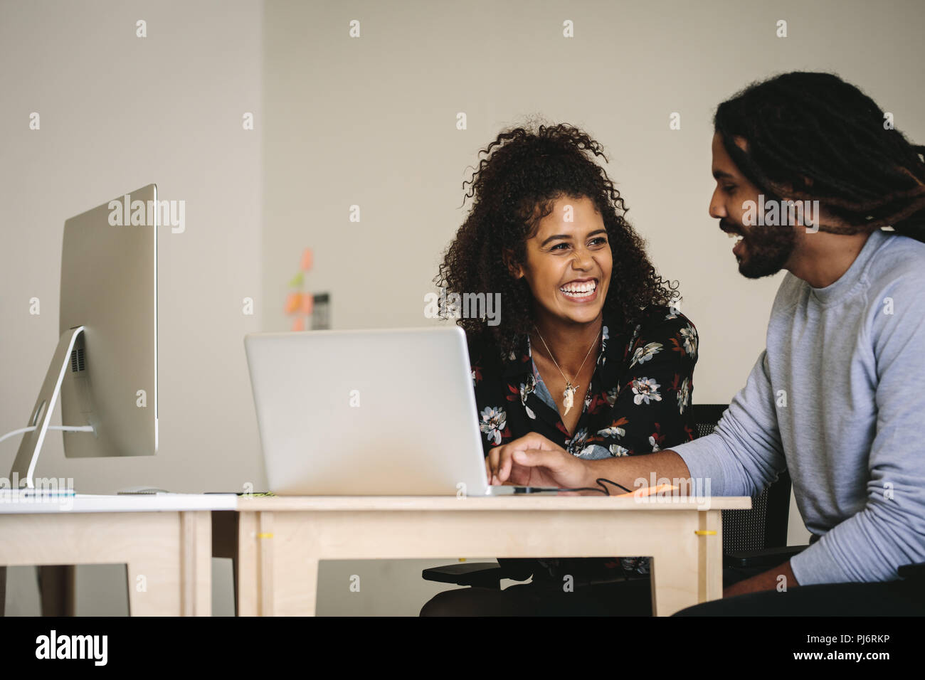 Imprenditore sorridente e la donna a discutere di lavorare seduto alla scrivania con computer portatile e un computer desktop. Sorridente imprenditrice a parlare con il suo collega un Foto Stock