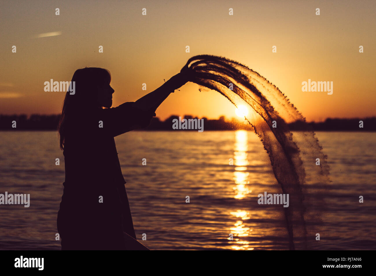 Donna che gioca con la sabbia sulla spiaggia con tramonto Foto Stock