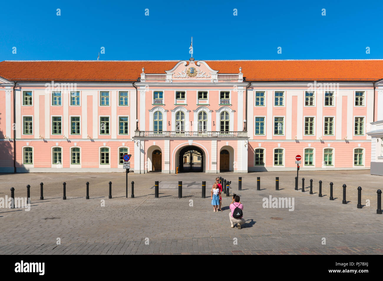 Foto di famiglia, vista di un uomo che scatta una foto di sua moglie e figlia contro la facciata rosa del castello di Toompea a Tallinn, Estonia. Foto Stock