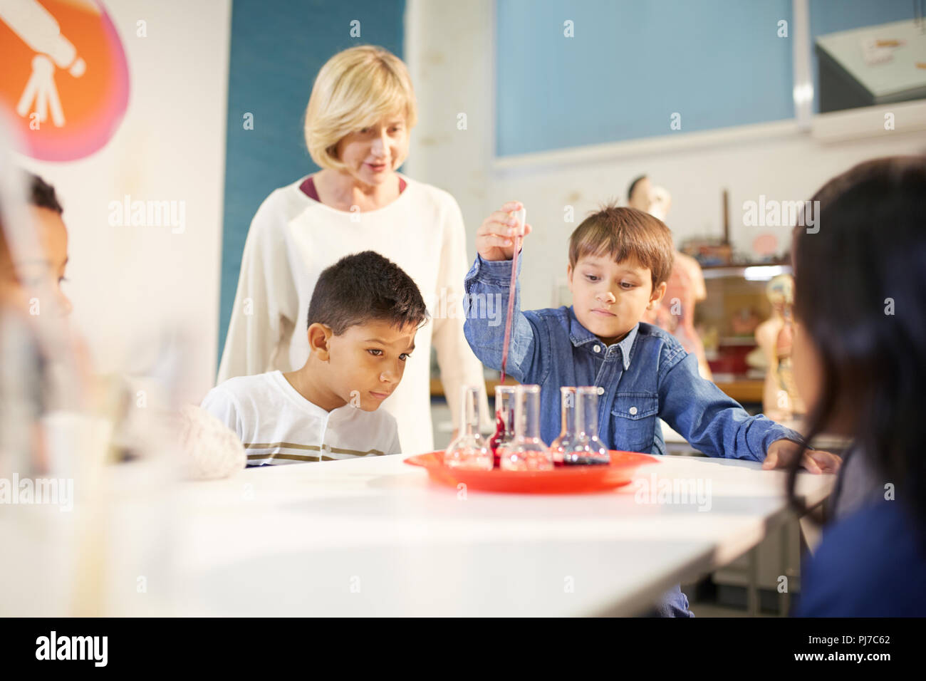 L insegnante e gli studenti usando una pipetta e bicchieri in mostra interattiva in science center Foto Stock