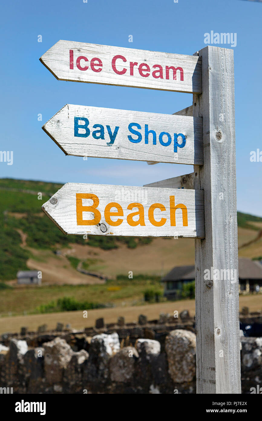 Segno posto a dare indicazioni al negozio di articoli da regalo e la spiaggia nel villaggio di Rhossili. Cielo azzurro sfondo in formato verticale. Foto Stock