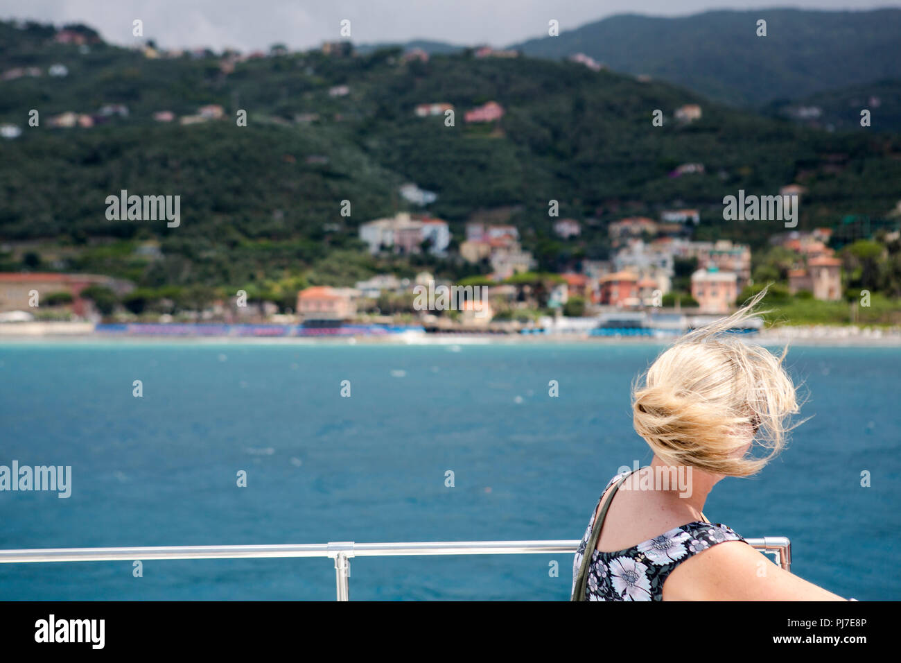 Una singola donna seduta sul ponte superiore di una barca del turismo con capelli biondi soffiando intorno selvaggiamente nel vento. Foto Stock