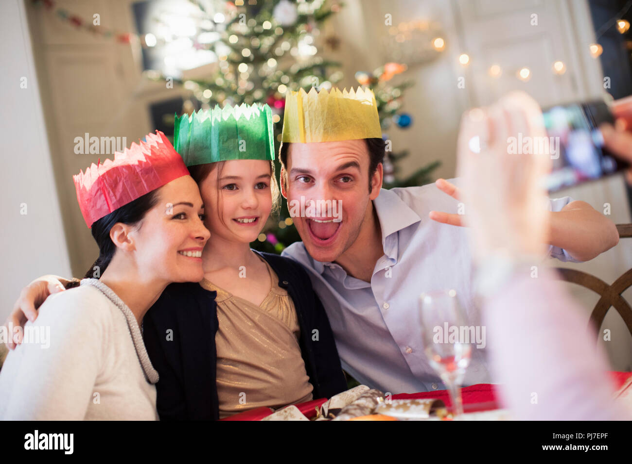 Famiglia giocoso in corone di carta che posano per una fotografia a Natale a tavola Foto Stock