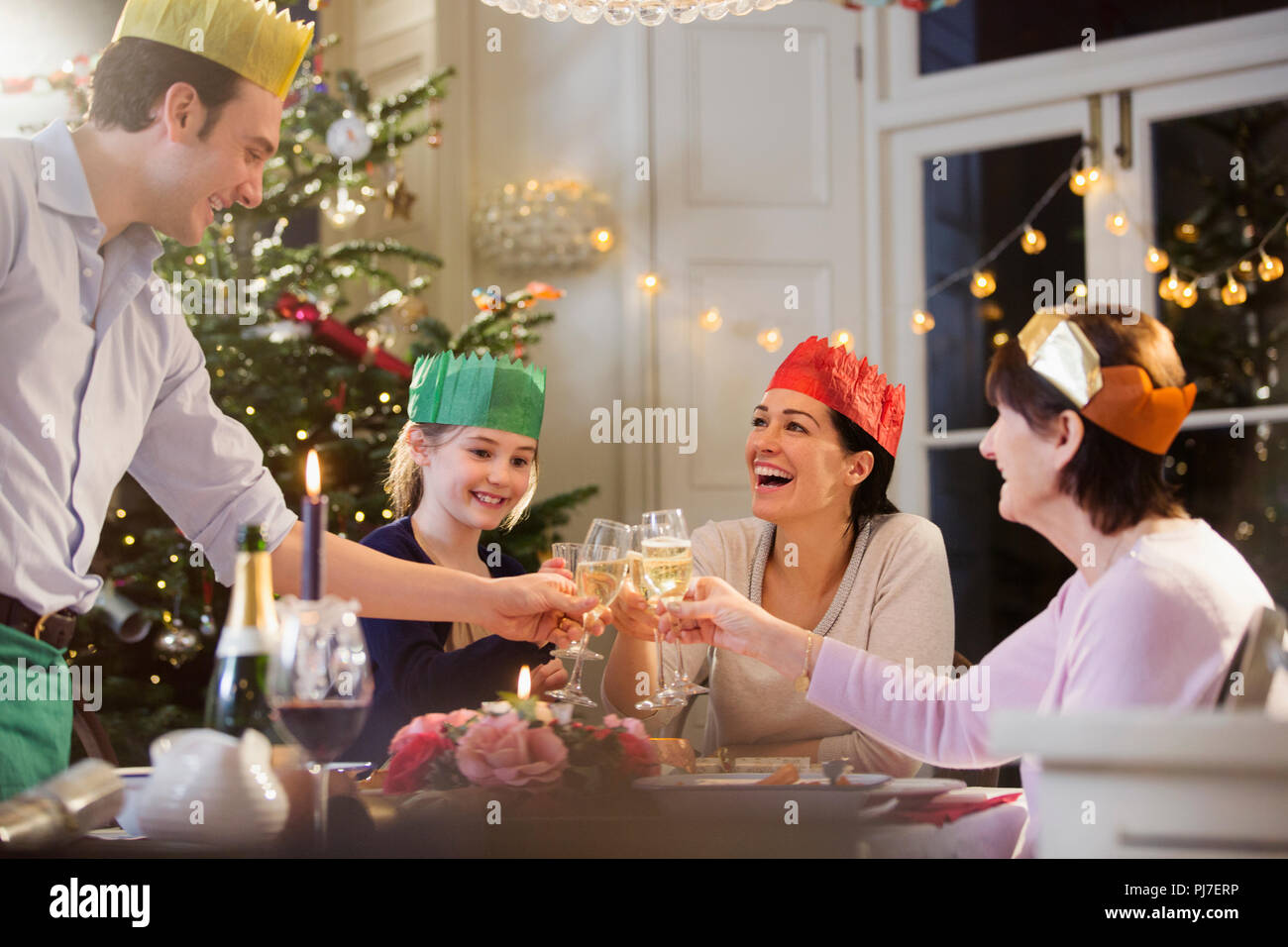 Multi-famiglia di generazione in corone di carta di tostatura flauti champagne a lume di candela la cena di Natale Foto Stock
