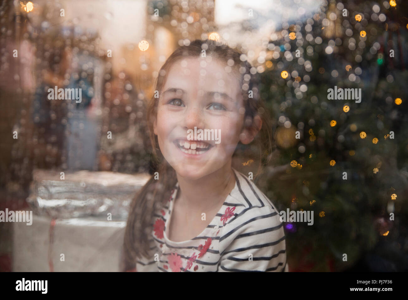 Ritratto felice ragazza alla finestra bagnato in Natale soggiorno Foto Stock