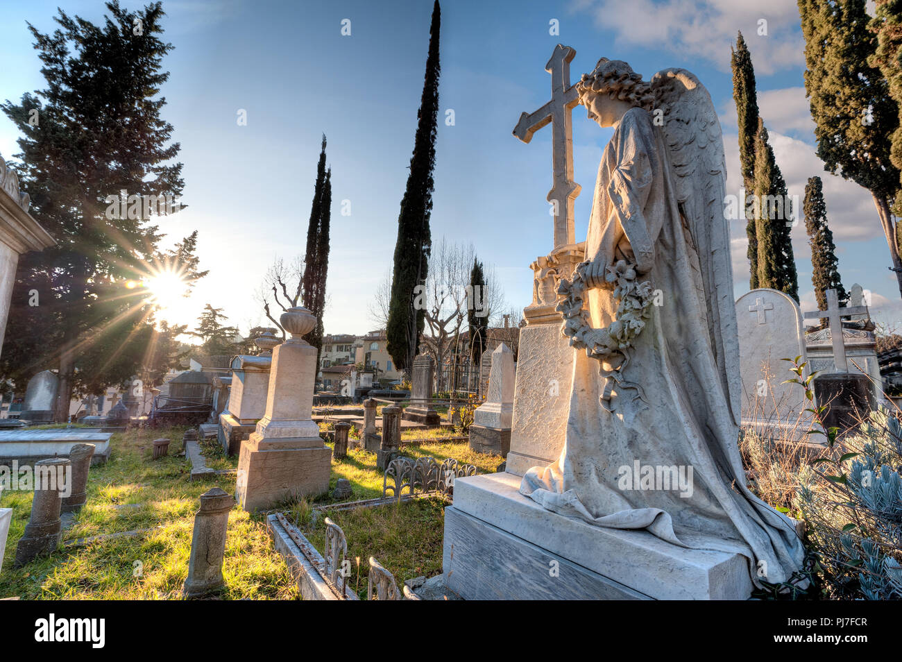 Un angelo di marmo con la sua mano sulla croce, rivolta verso il sole, tra le tombe del cimitero, in concentrazione, tenendo una corona Foto Stock