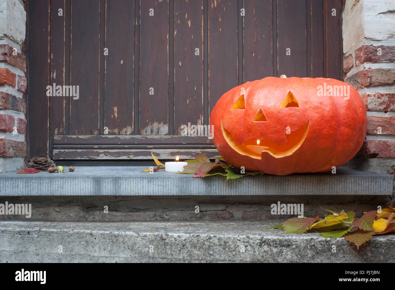 Un allegro jack-o-lantern sorrisi su un autunno porta con una candela, pronto per la festa di Halloween. Foto Stock