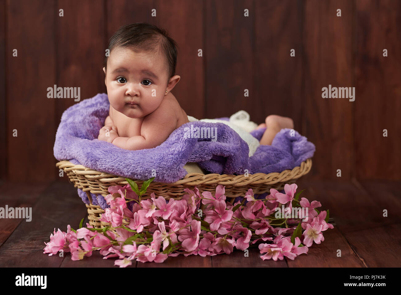 Baby girl lay in cesto guardano alla fotocamera su scuro dello sfondo in legno Foto Stock