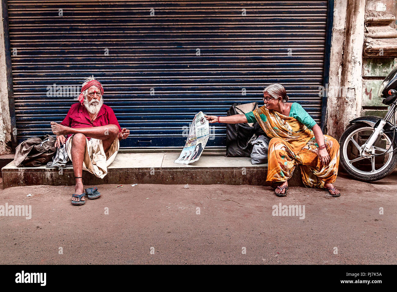 Senior Citizen donna leggendo il giornale e senior citizen uomo seduto vicino a. La foto è stata scattata in estate nella città di Ahmedabad Foto Stock