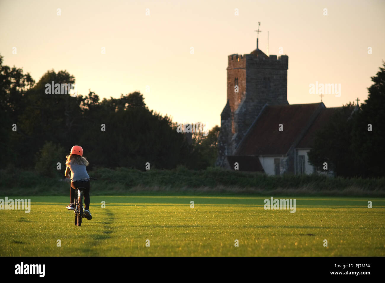 Ragazza in bicicletta nella campagna vicino a una chiesa del paese Foto Stock