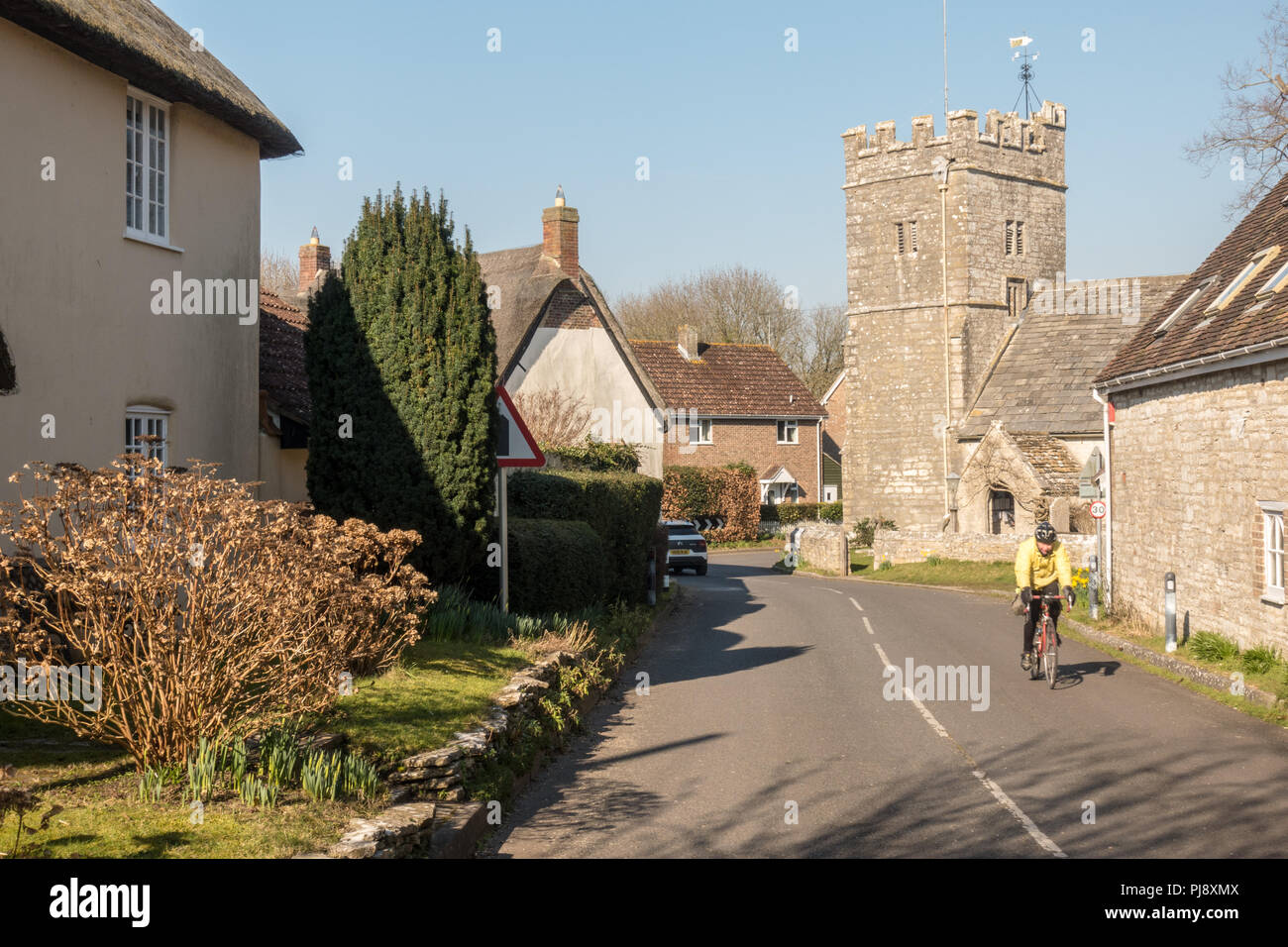 Dorchester, England, Regno Unito - 24 Febbraio 2018: Un ciclista passa la tradizionale chiesa parrocchiale di West Stafford villaggio nel Dorset. Foto Stock