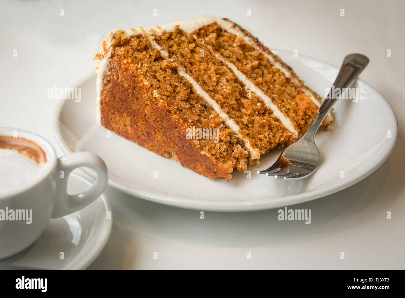 Una fetta di umido e una deliziosa torta di carote con una tazza di caffè sul lato Foto Stock