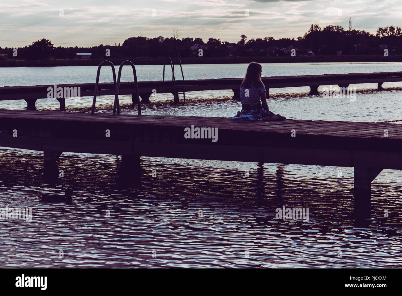 Femmina giovane ragazza seduta sul molo in legno guardando l'acqua Foto Stock