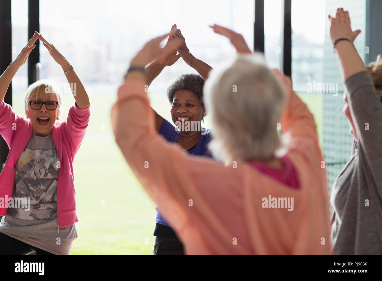 Felice senior attivo delle donne che esercitano, bracci di estensione in testa nella classe di esercizio Foto Stock