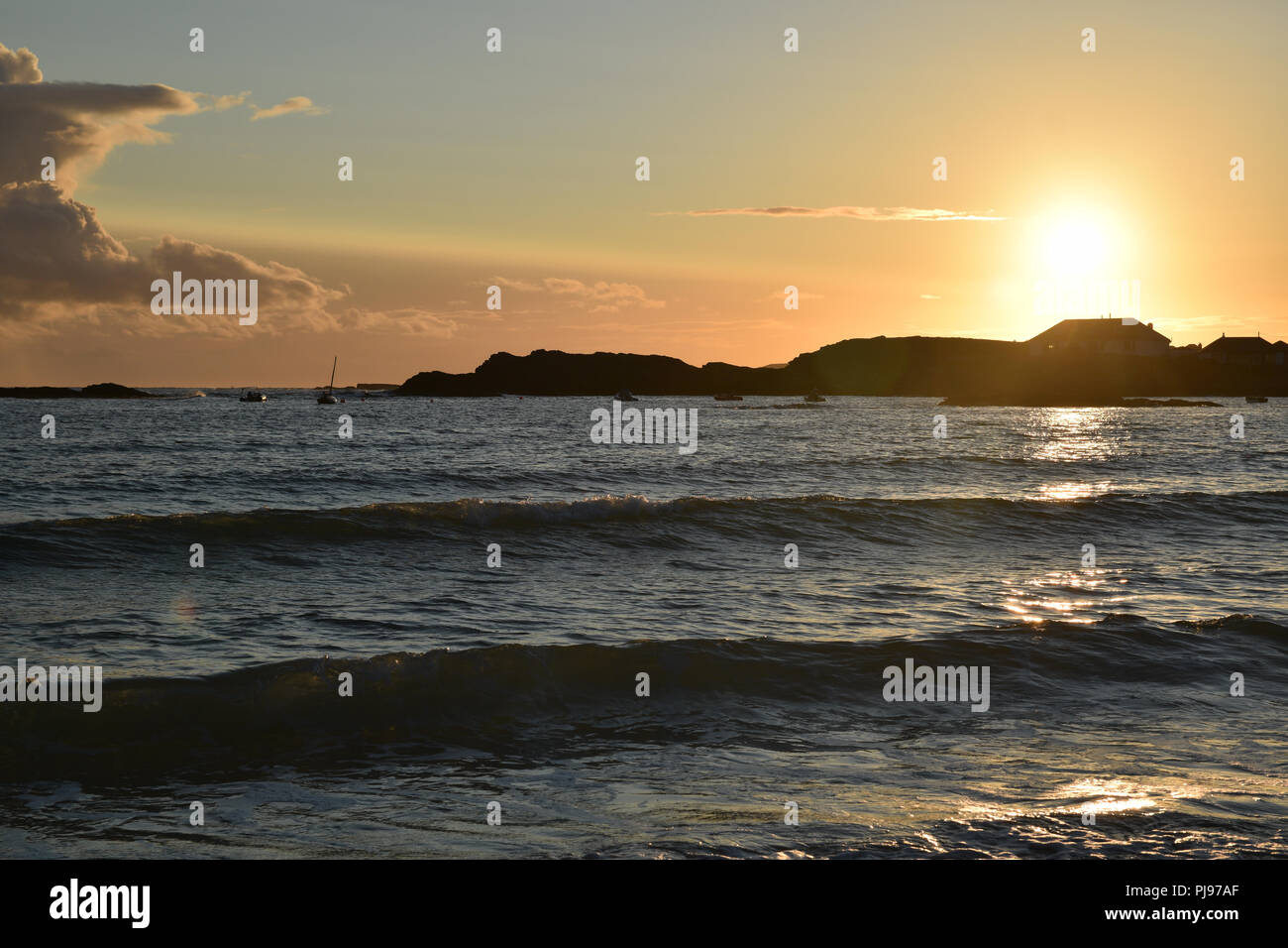 Sunset over Trearddur Bay vicino a Holyhead, Anglesea, il Galles del Nord con la luce del sole che si riflette sull'acqua e onde. Orange sky silhouette seasc paesaggio Foto Stock