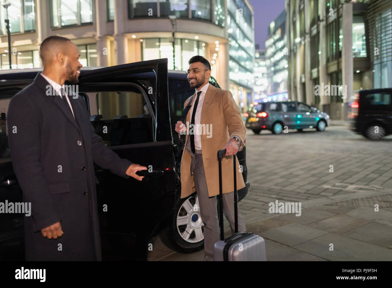 Apertura del driver della porta auto per l uomo d affari con la valigia sulla strada urbana di notte Foto Stock