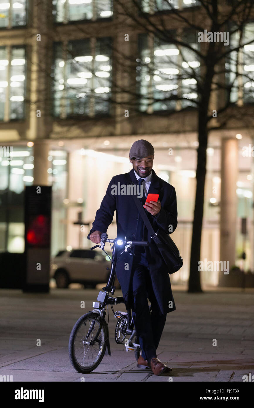Imprenditore con bicicletta utilizzando smart phone sul marciapiede urbano di notte Foto Stock