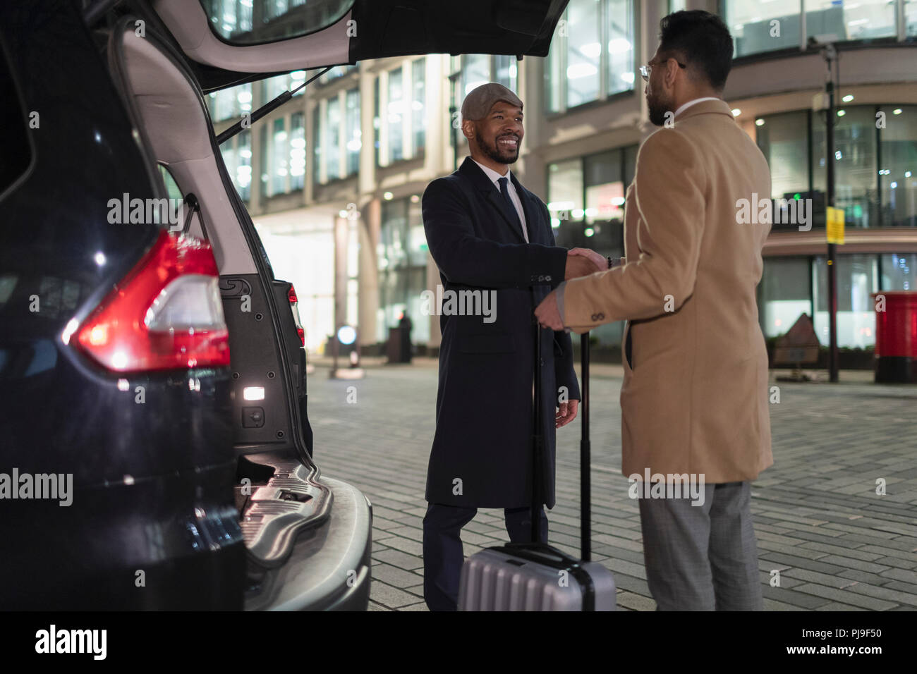 Imprenditori con la valigia lo handshaking sul retro delle auto sulla strada urbana di notte Foto Stock