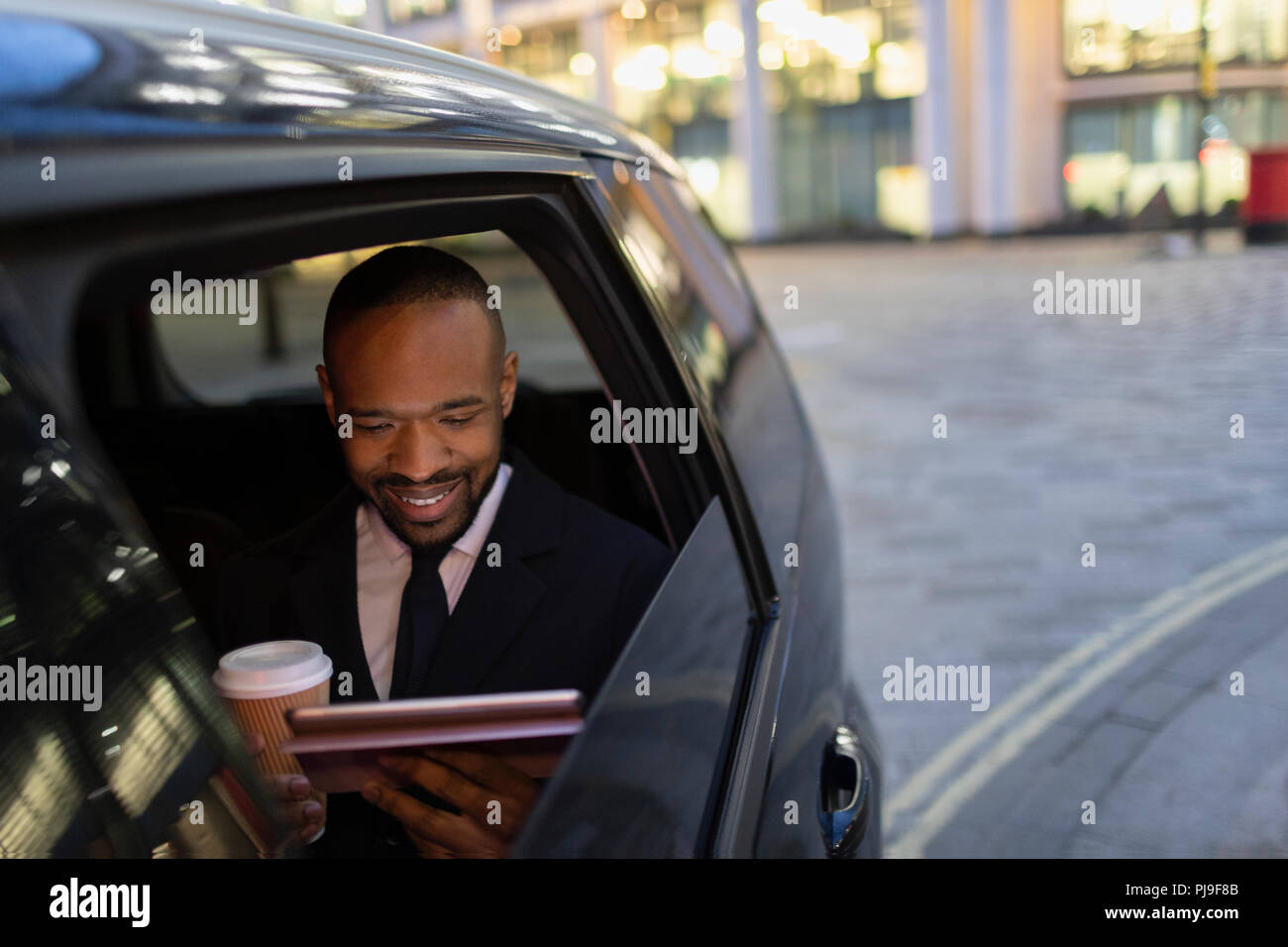 Imprenditore a bere caffè e con tavoletta digitale in taxi crowdsourced Foto Stock