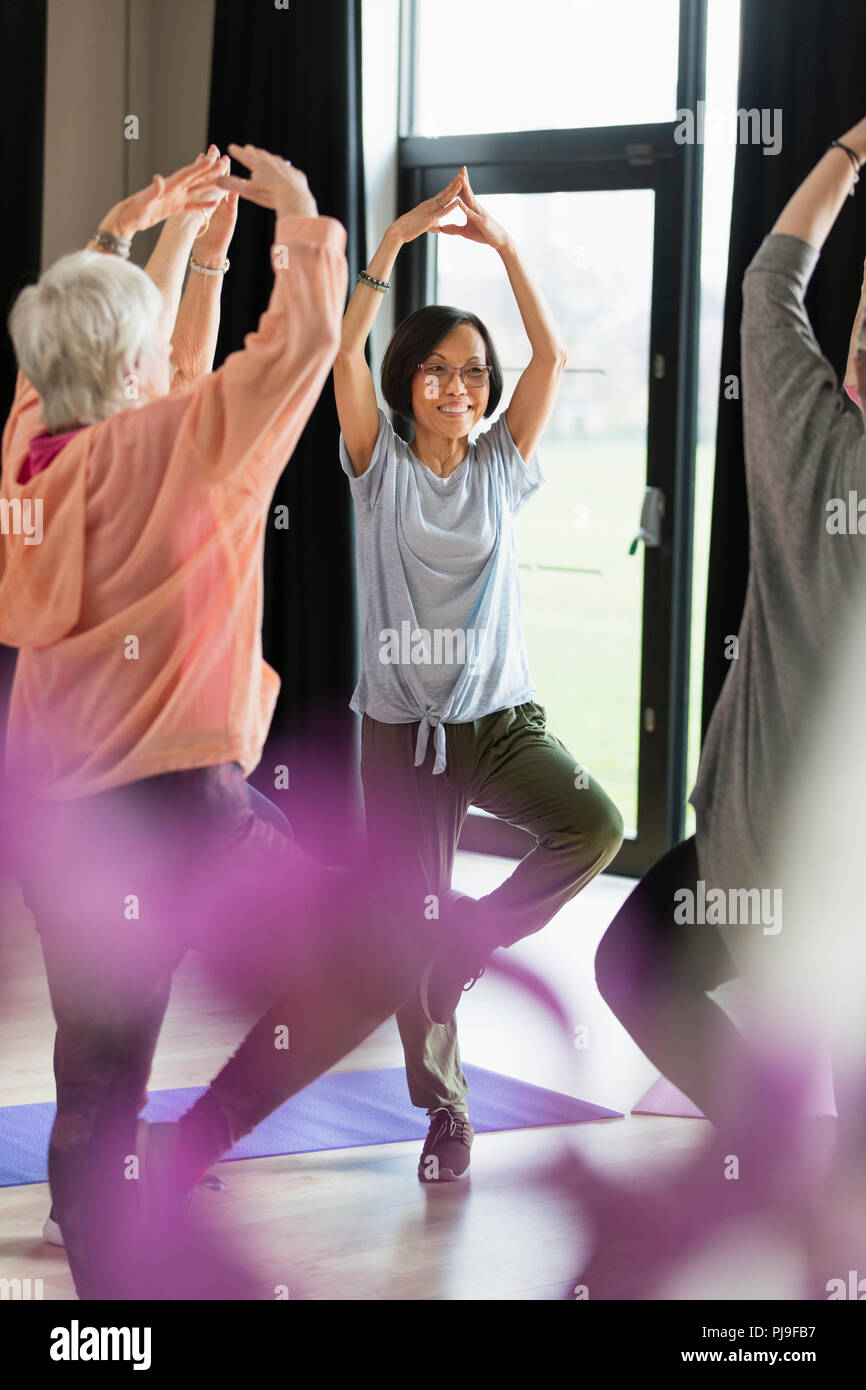Sorridente senior attiva donna esercita la pratica dello yoga posa ad albero Foto Stock