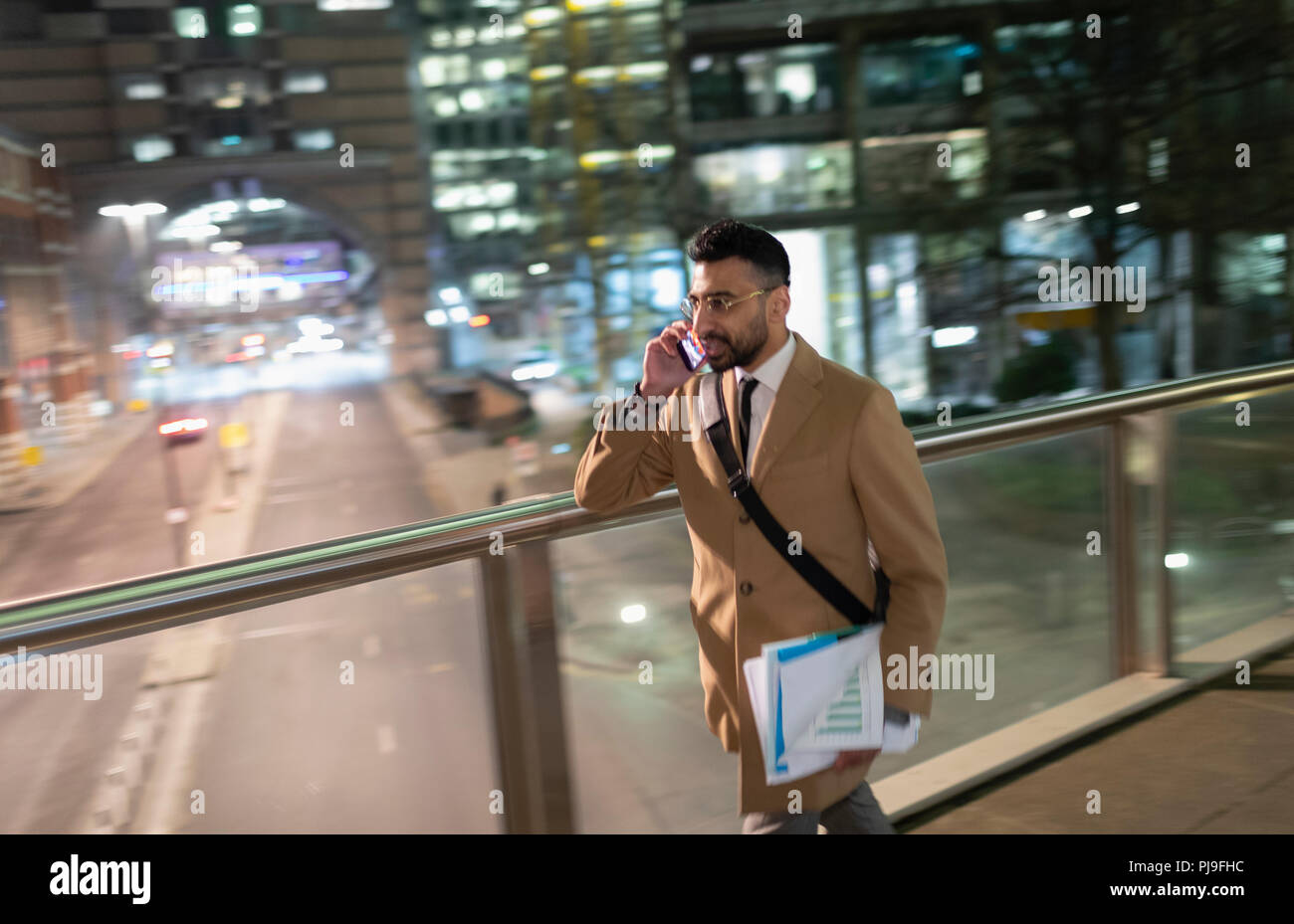 Imprenditore parlando su smart phone, camminando su urban ponte pedonale di notte Foto Stock