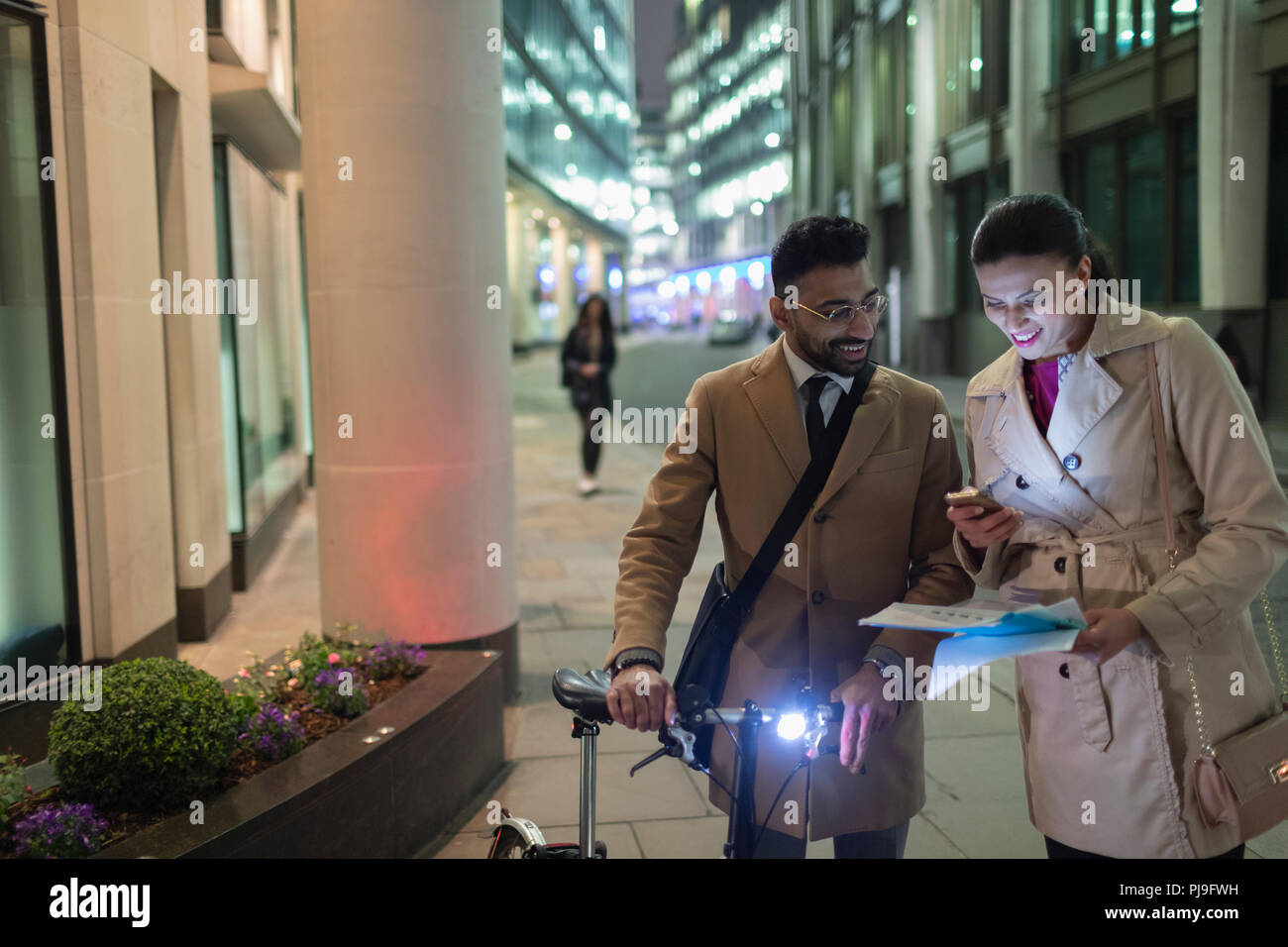 La gente di affari con smart phone e le biciclette a rivedere la documentazione sulla strada urbana di notte Foto Stock