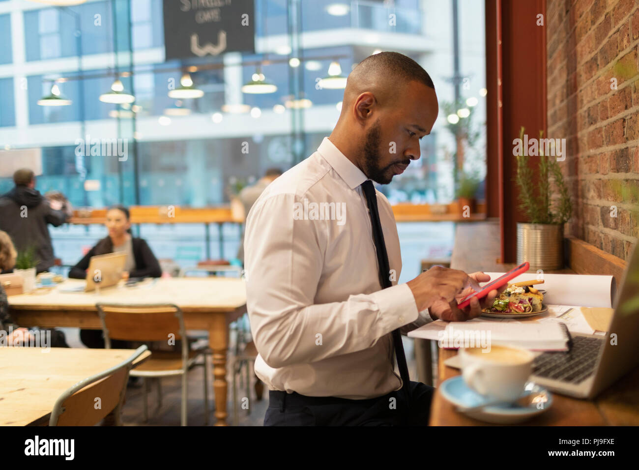 Imprenditore utilizzando smart phone e mangiare il pranzo al cafe Foto Stock