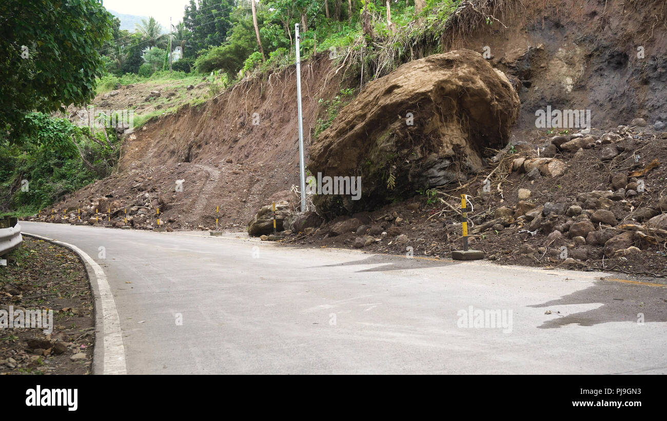 Smottamenti e frane sulla strada di montagna. Fango e rocce bloccando la strada.distrutto strada rurale frana danneggiato nel proiettore potente. Collassato su per la montagna. Filippine, Camiguin. Foto Stock