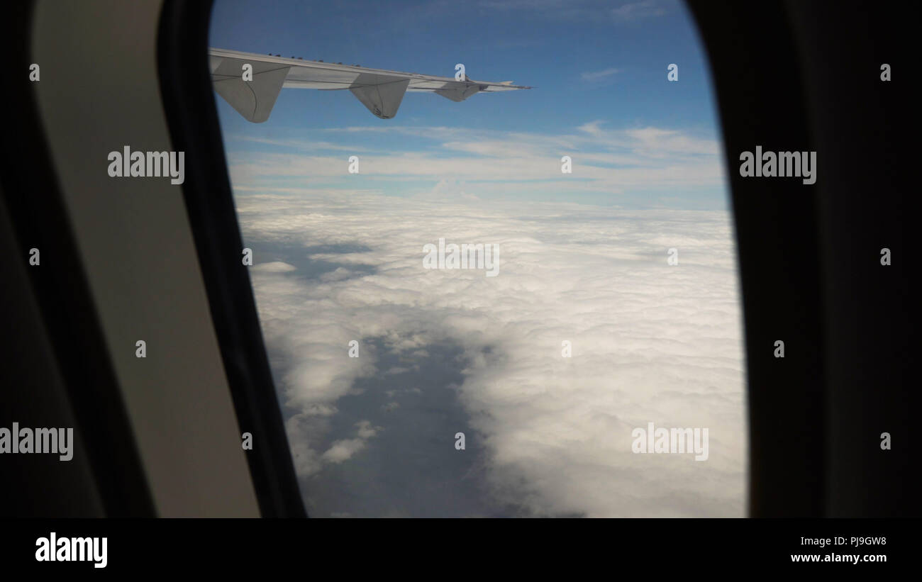 Vista attraverso un aereo finestra sull'isola tropicale, oceano e Cielo e nubi. Vista aerea del mare, le nuvole e il cielo come visto attraverso la finestra di un aeromobile. Concetto di viaggio. Foto Stock