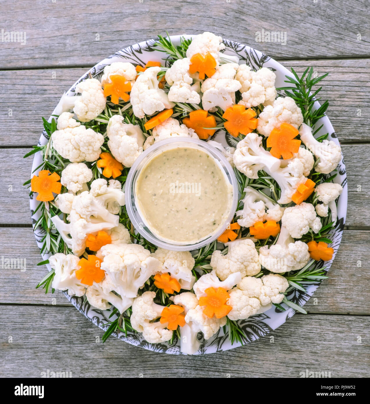 Festive cibo crudo vegano piatto di verdure con hummus dip: cime di cavolfiore, carote tagliate in forme a fiore e rosmarino Foto Stock