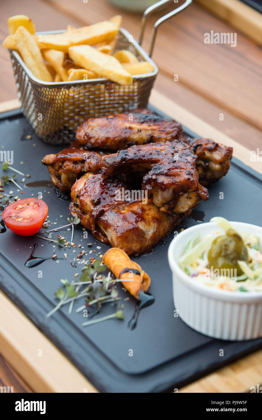 Deliziosi barbecue ali di pollo servito con insalata Coleslaw e patatine fritte sul bordo di taglio Foto Stock
