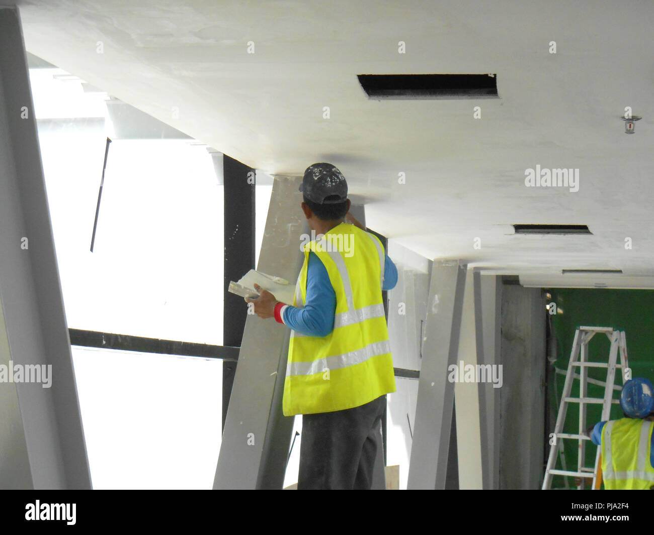 Sito in costruzione i lavoratori stanno facendo intradosso soffitto foglietta lavoro presso il sito di costruzione. Base e finale dello strato di rivestimento di applicare per ottenere la superficie liscia. Foto Stock