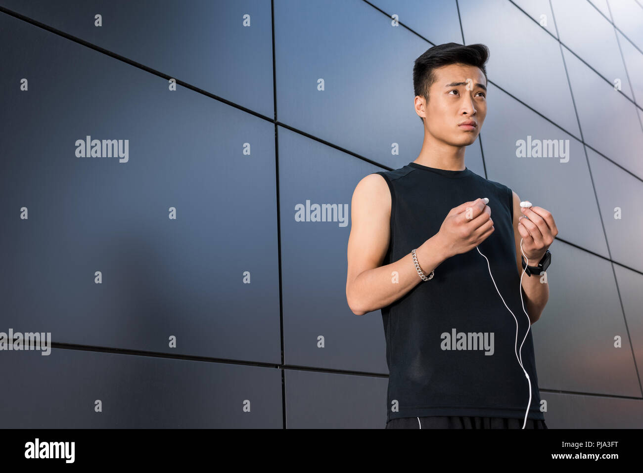Giovani asiatici sportivo mettendo su auricolari in corrispondenza via della città Foto Stock