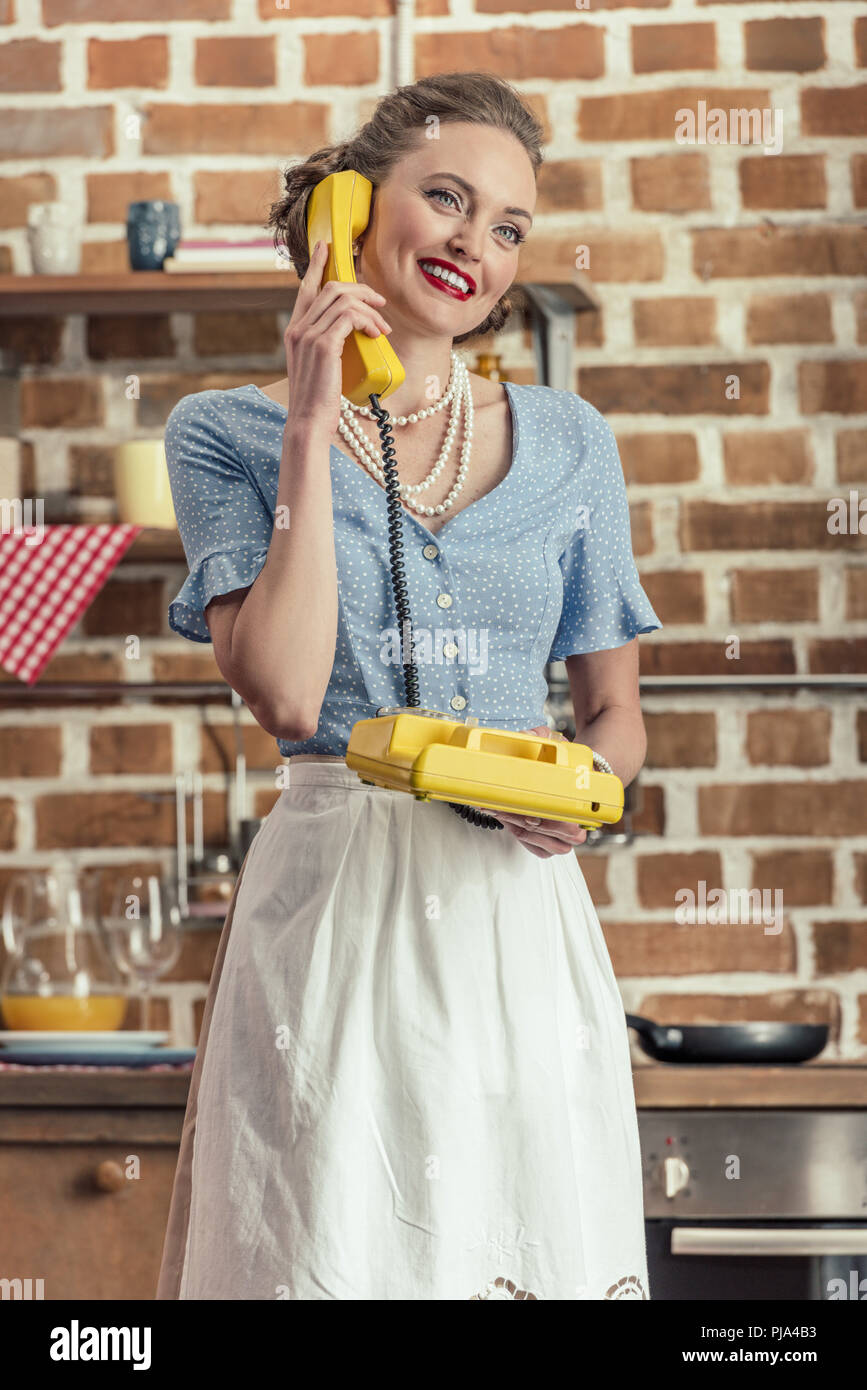 Bella casalinga felice di parlare per annata telefono rotante in cucina Foto Stock