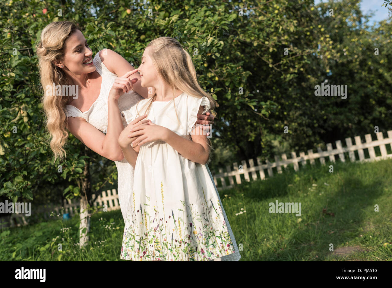 La bionda mamma e figlia in abiti bianchi divertirsi in giardino rurale Foto Stock