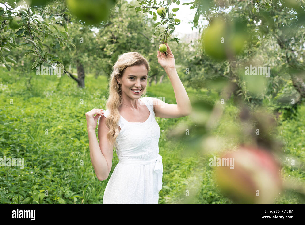 Donna sorridente in abito bianco di trascorrere del tempo nel giardino di Apple Foto Stock