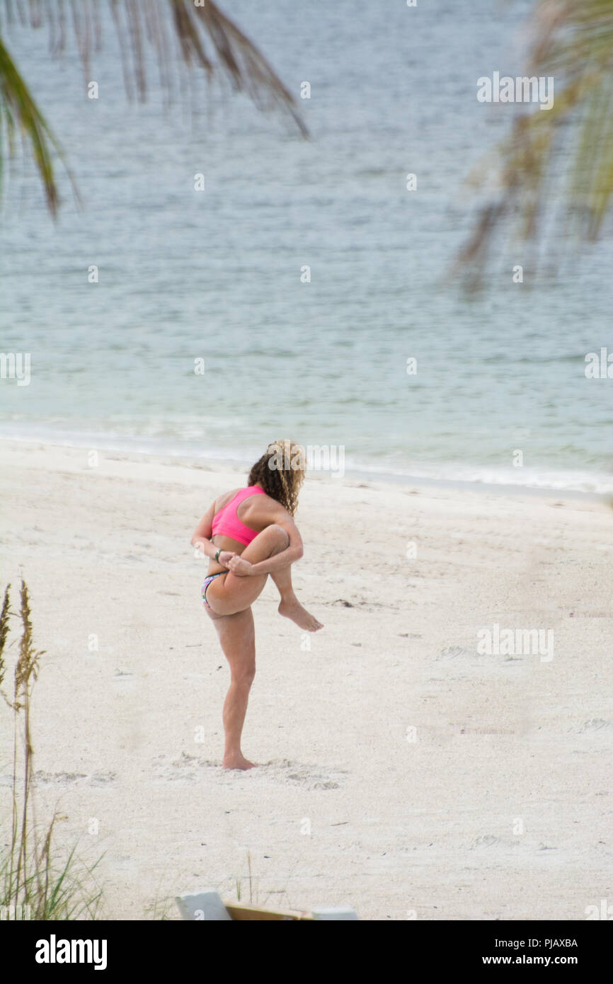 Una giovane donna svolge un complesso permanente pongono yoga con la gamba in aria sulla spiaggia di Anna Maria Island, Florida. Foto Stock