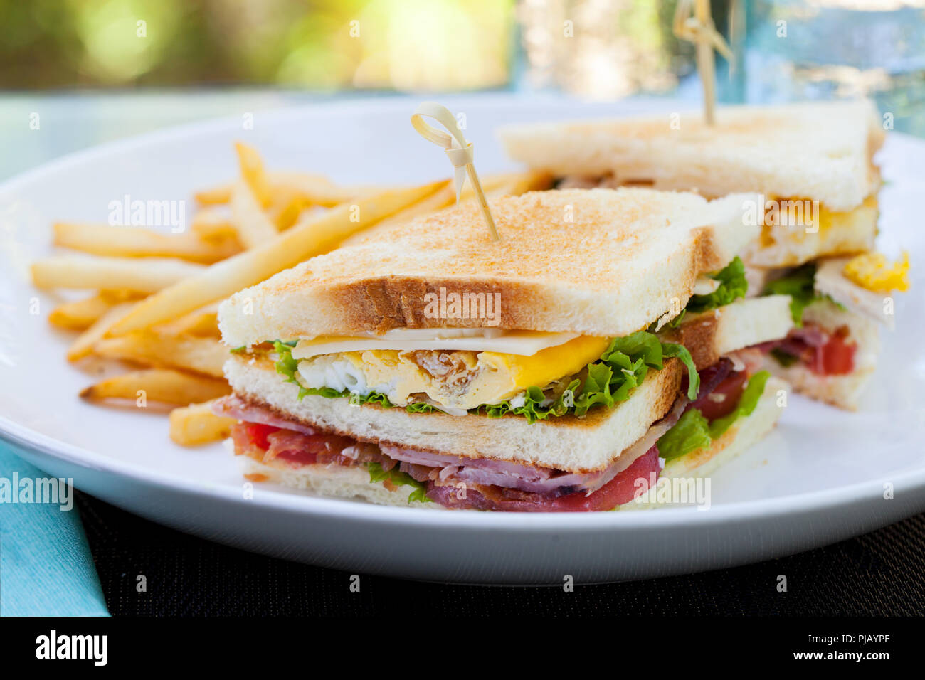 Club sandwich con patatine fritte su una piastra bianca. Estate sfondo all'aperto. Foto Stock