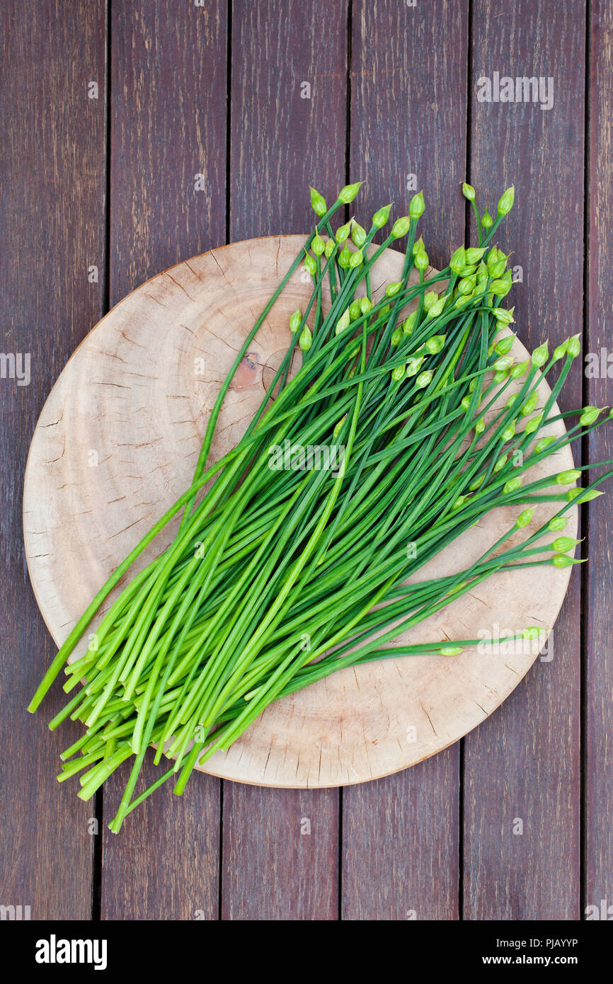 Fiore di erba cipollina, erba cipollina aglio cinese o erba cipollina su un tagliere. Sfondo di legno. Vista dall'alto. Foto Stock