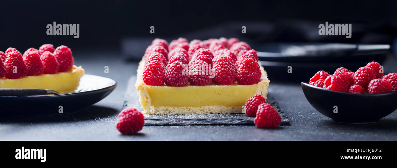 Lampone crostata con crema alla vaniglia e cioccolato bianco sulla scheda di ardesia. Pietra nera dello sfondo. Copia dello spazio. Foto Stock