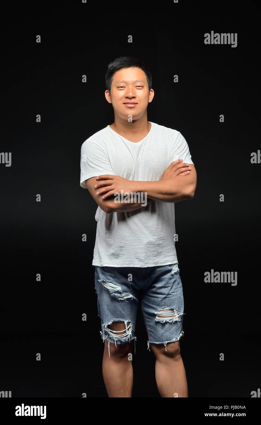 Ritratto di un maschio di studenti asiatici di apparizione su uno sfondo nero che sta con le mani giunte Foto Stock