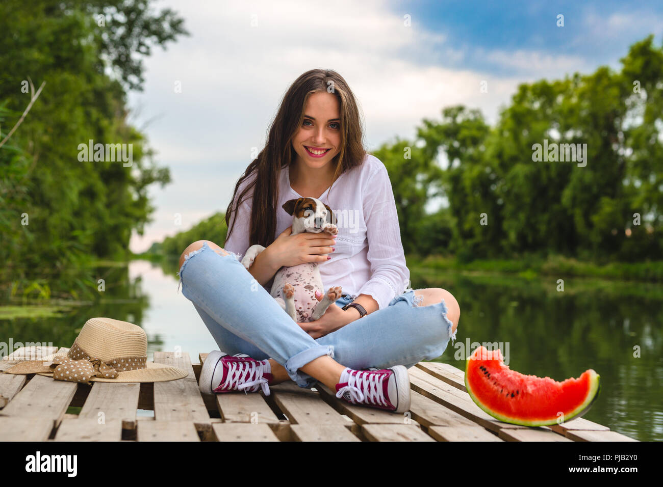 Donna godendo giornate estive con il suo cucciolo , seduta sul fiume dock Foto Stock