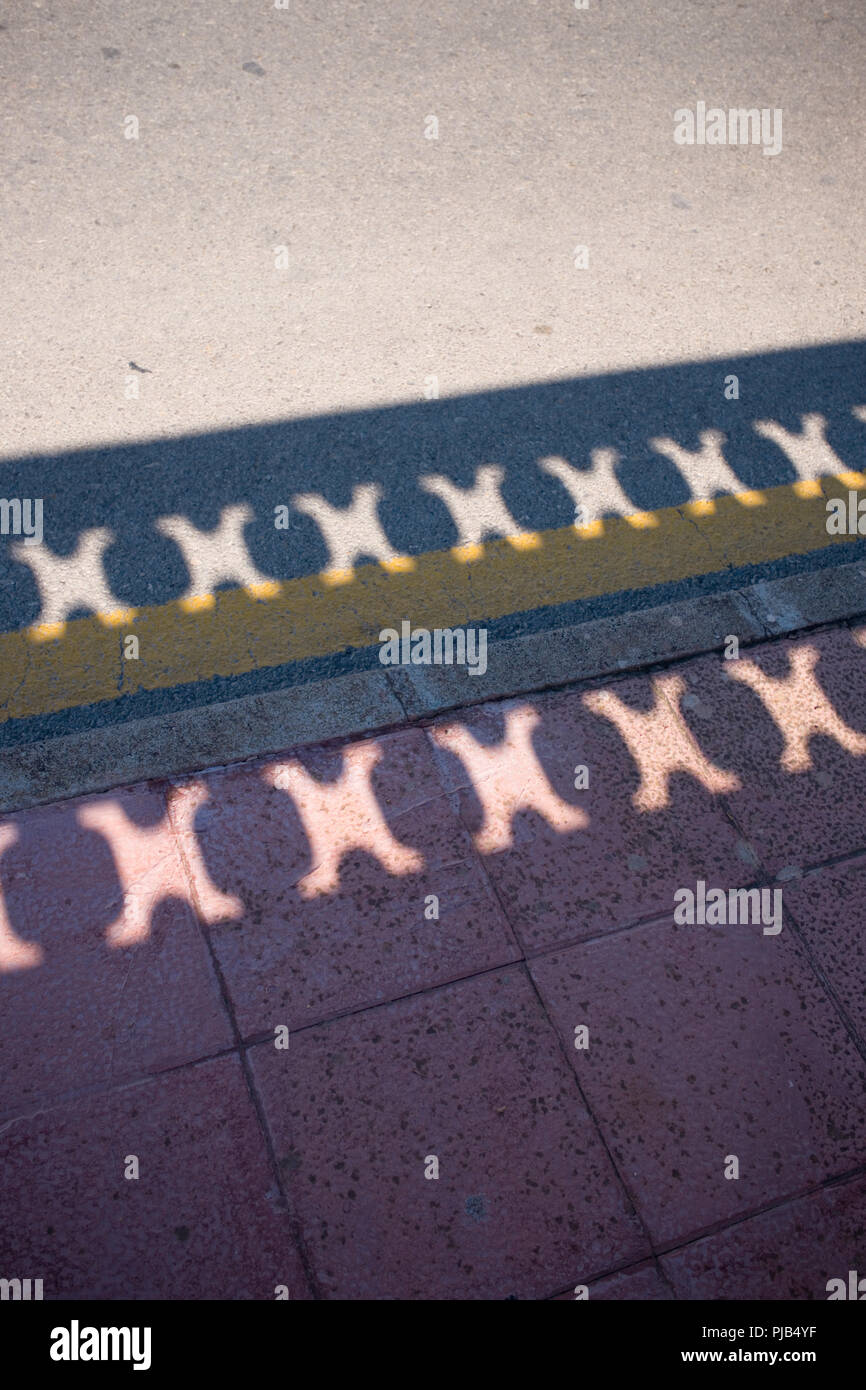 Guardando verso il basso in corrispondenza di ombre di un terrazzo parete su un marciapiede e strada in Spagna Foto Stock