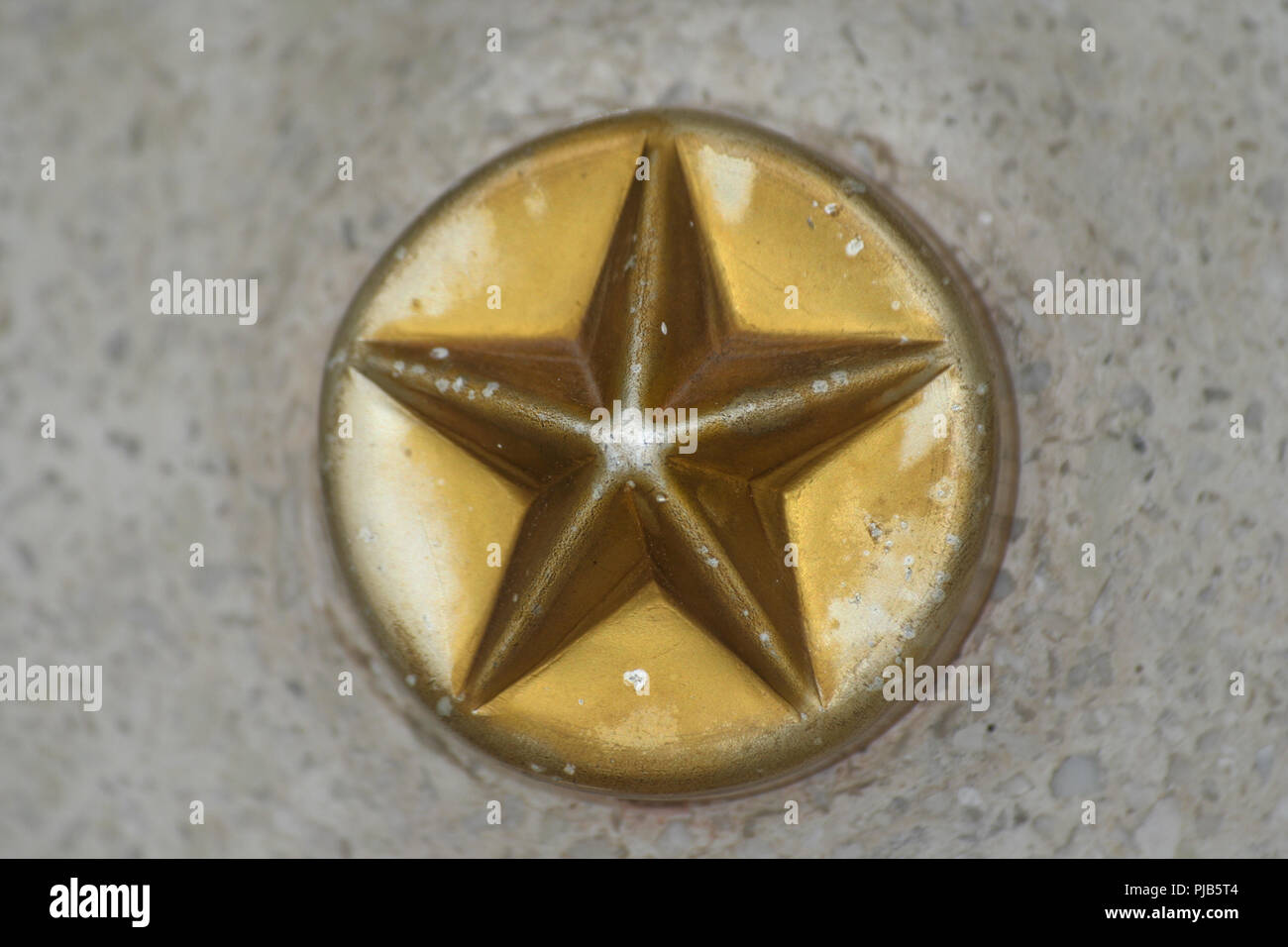 Un bel close-up di a cinque punte stella di metallo su un cerchio annegato nel calcestruzzo. Il colore oro sbiadito un po'. Foto Stock