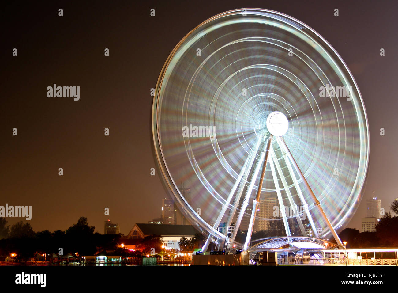 Una grande esposizione lunga inquadratura di un illuminato di filatura ruota panoramica Ferris di notte in Malaysia. Foto Stock
