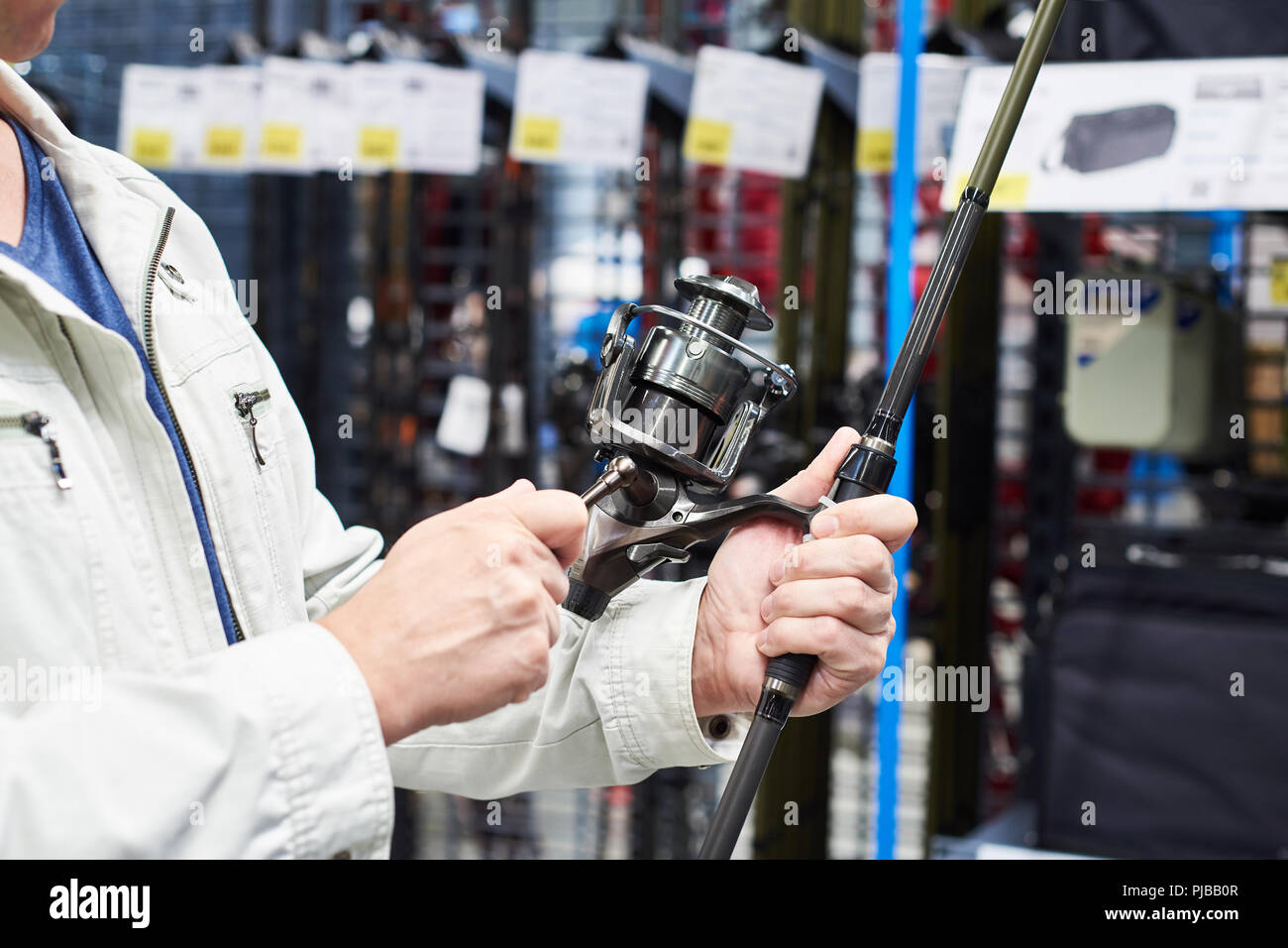 Uomo sceglie la canna da pesca nel negozio di articoli sportivi Foto Stock