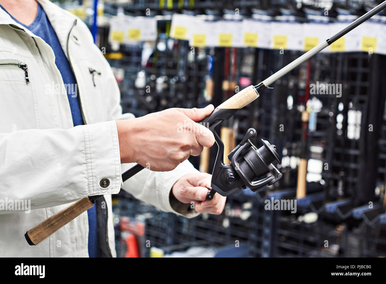 Uomo sceglie la canna da pesca nel negozio di articoli sportivi Foto Stock
